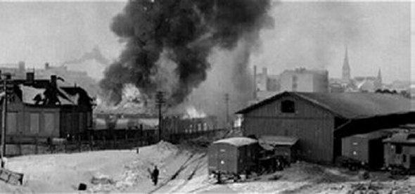 asemapihaa raiteineen, junavaunuja, joiden takana savupatsas.