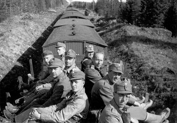 Juna kulkee metsän reunustamaa rataa, ja sen katolla istuu miehiä.